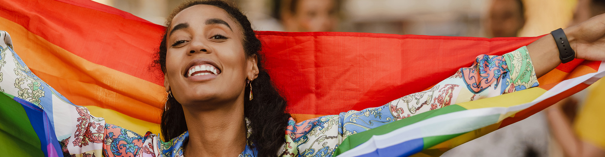Black woman smiling and holding rainbow flag during pride parade